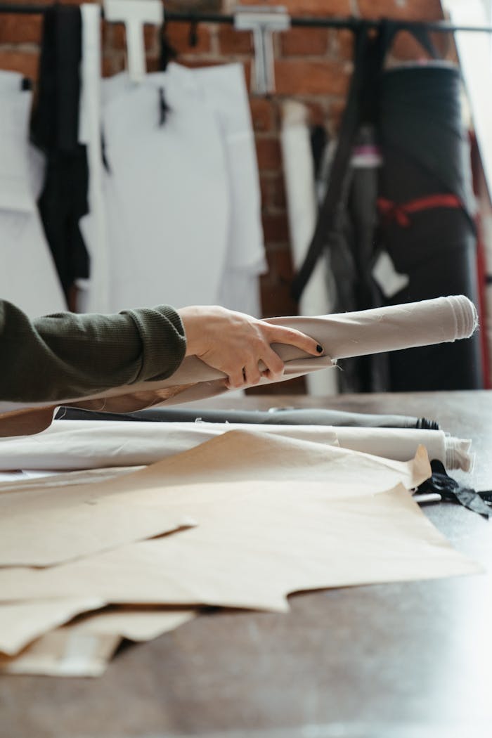 A close-up of hands holding fabric rolls in an organized tailoring workspace.