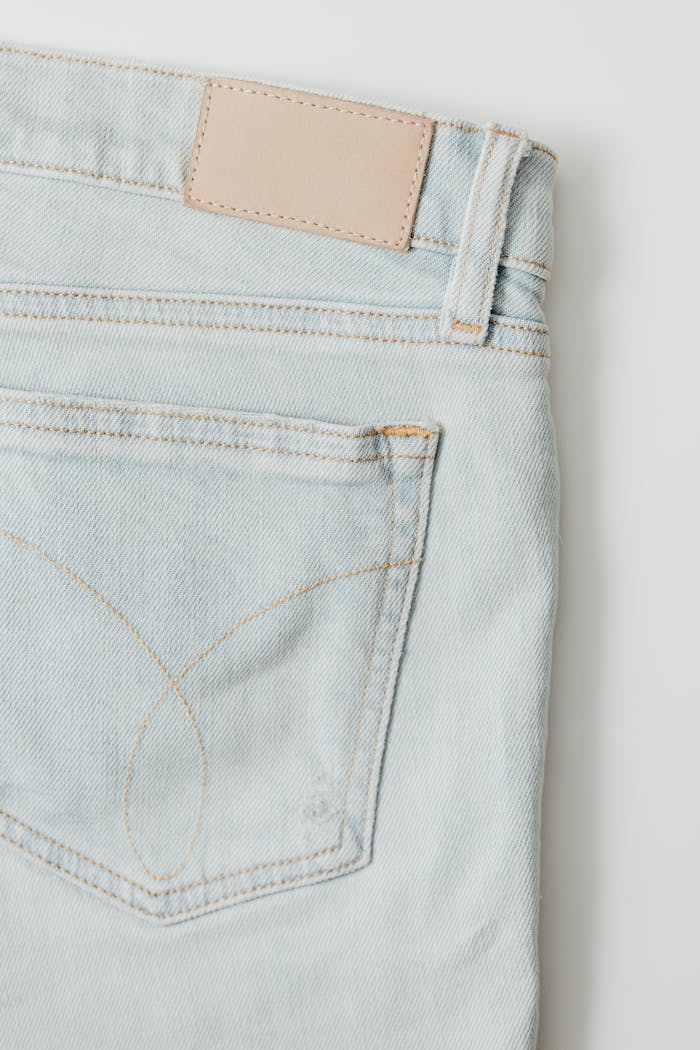 Close-up of light blue denim fabric with stitching details, ideal for fashion use.