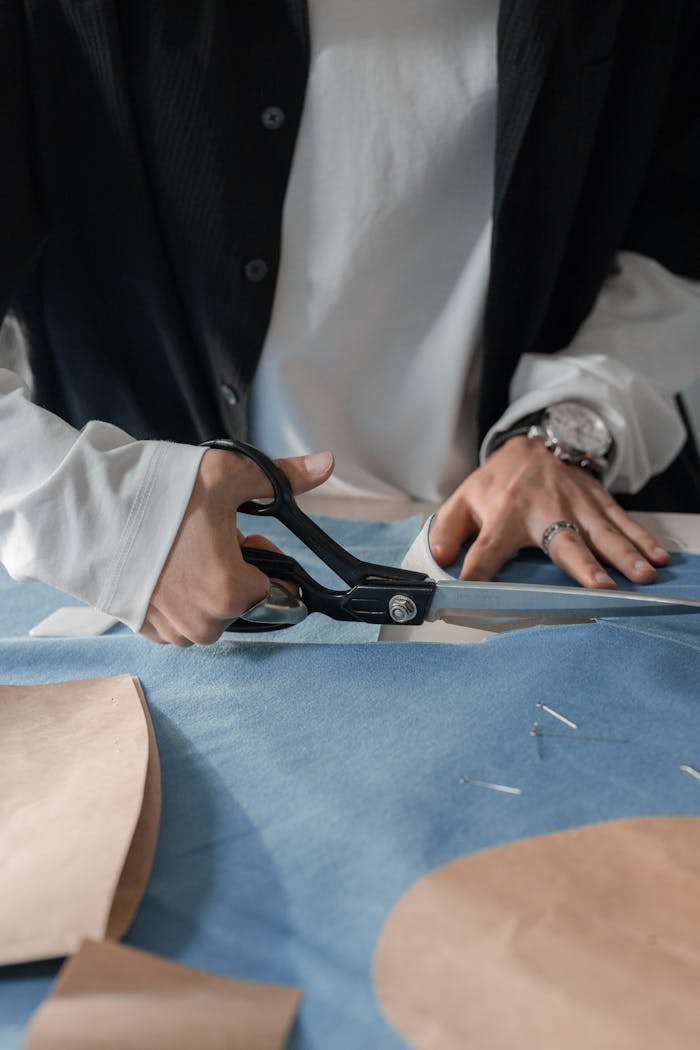Fashion designer cutting fabric with precision using scissors on a pattern table.